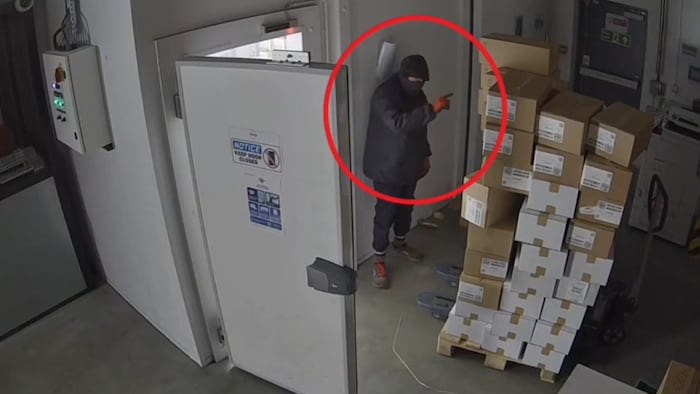 A man covering his face stands counting cardboard boxes piled up in a storage room