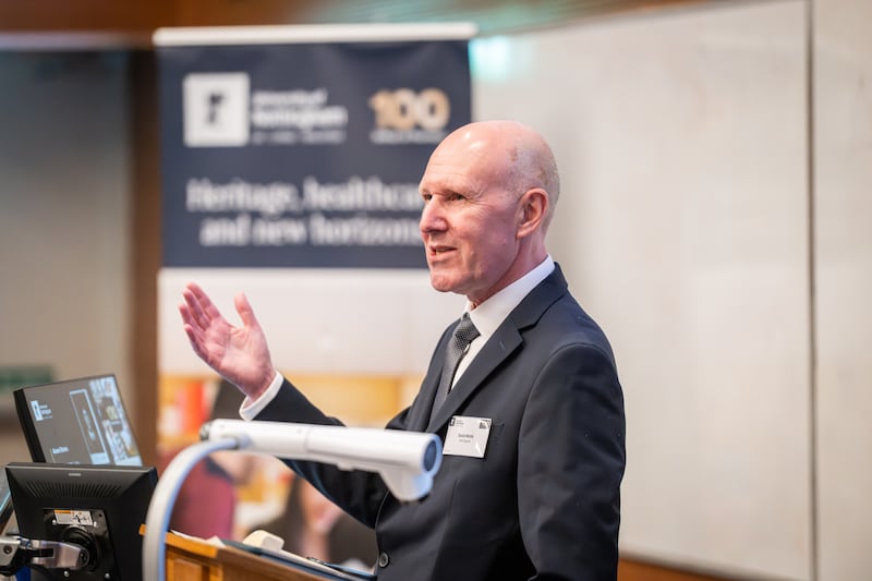 a bald white man raises his hand as he talks to a sat-down audience