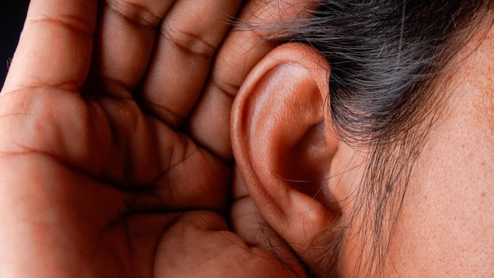 close up of person's hand placed behind their ear to signal they are listening.