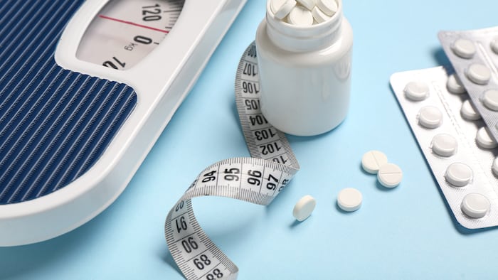 Bottle of white pills alongside weighing scales and measuring tape