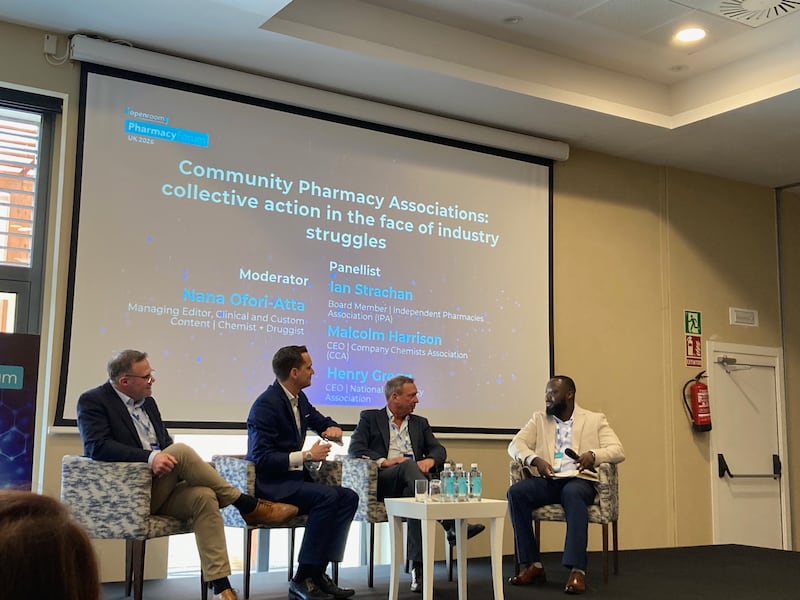Four men sit down on a stage discussing community pharmacy