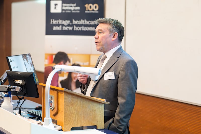 a white man wearing a grey suit and tie with grey hair speaks to an audience