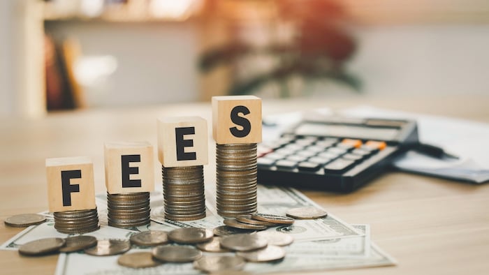 "Fees" spelled out in block letters on stacks of coins. Coins sit on top of paper bills with a calculator.