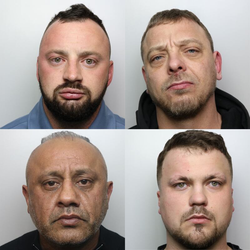 Four men face the camera not smiling. 3 men are white with short haircuts and facial hair. 1 man is brown with very short hair and stubbled facial hair.