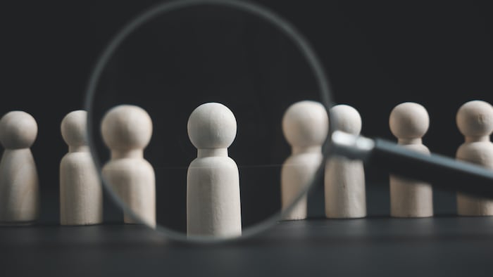 Magnifying glass over wooden figurines on black background