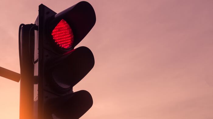 Red traffic light on sunset sky background.