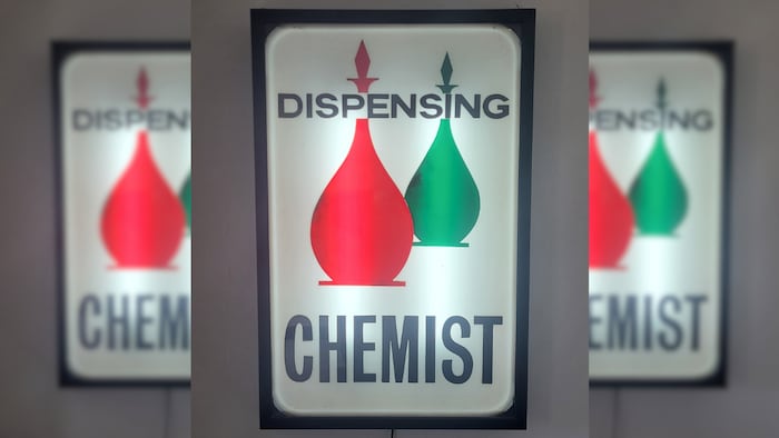 A lit-up sign with a red and green glass bottle image behind the words 'dispensing chemist'
