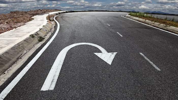 A U turn arrow traffic symbol imprint on a lonely asphalt road against a blue cloudy sky. - Image