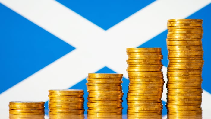 coins piled up in ascending order in front of a scotland flag