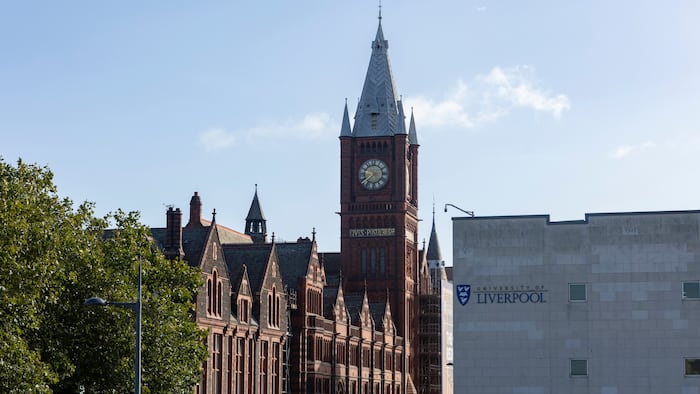 a grey building in the foreground with the university of liverpool written on it and a red brick building behind it with a clock tower